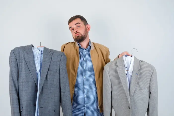Young man in jacket, shirt puzzled with choosing a suit and looking thoughtful , front view