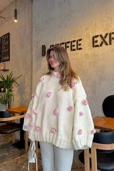 Person in a café wearing a white oversized sweater with pink floral embellishments, highlighting unique sweater styles for cozy fashion.