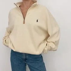 Model wearing a cream quarter-zip pullover sweater with a small embroidered logo, paired with jeans, showcasing casual sweater styles for everyday fashion.