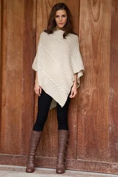Model wearing a cream cable knit poncho sweater with a draped fit, paired with black pants and brown boots, showcasing unique sweater styles for cozy fashion.