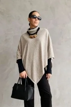 Model wearing a beige poncho sweater with a high neck, layered over a black top, showcasing elegant types of sweaters for stylish layering.