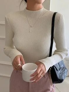 Person in a cream ribbed turtleneck sweater holding a white mug, paired with pink pants, highlighting cozy types of sweaters for winter fashion.