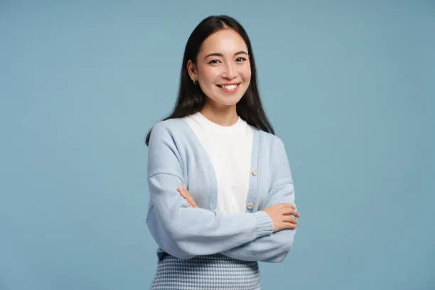 Person wearing a light blue cardigan over a white shirt, standing with arms crossed against a blue background.