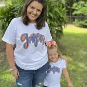 Smiling mother and daughter in matching “Gators” printed white T-shirts, created by a family clothing manufacturer.